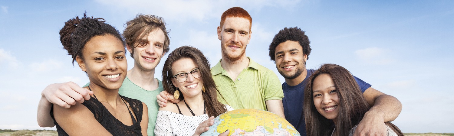 Sechs lächelnde junge Menschen unterschiedlicher internationaler Herkunft halten eine Weltkugel in der Hand.