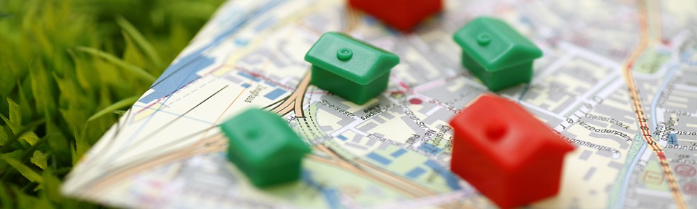 Nahaufnahme einer Stadtkarte mit Monopoly-Häuschen (Grün) und Hotels (Rot) drauf, welche auf einer Wiese liegt.
